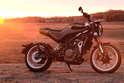 a motorcycle parked in a field with the sun setting in the background